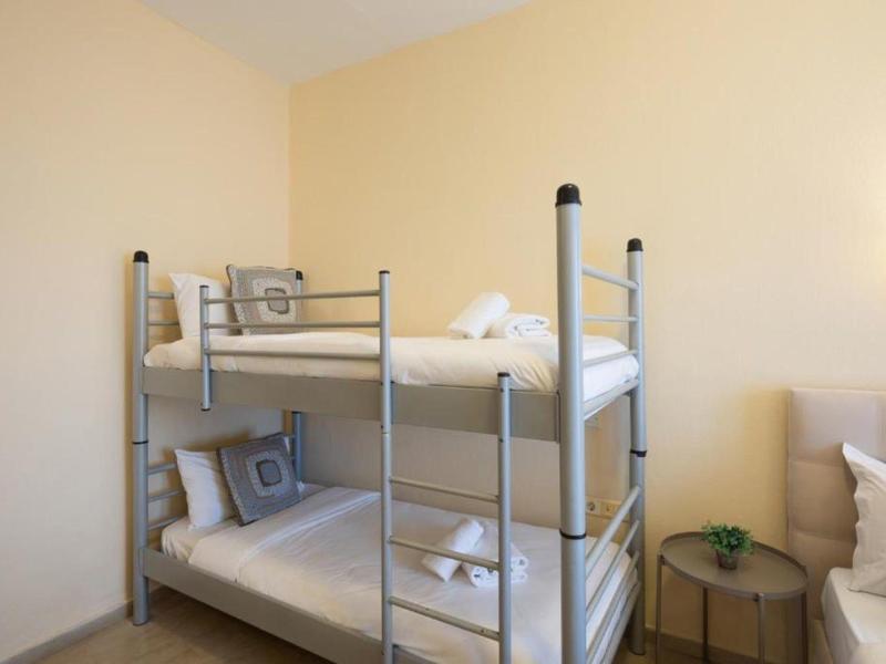 Prosty pokój z metalowymi łóżkami piętrowymi i neutralnymi ścianami.