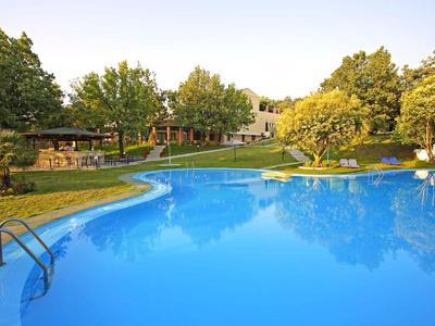 Grande piscina all'aperto con acqua limpida, circondata da prato e alberi in un hotel.
