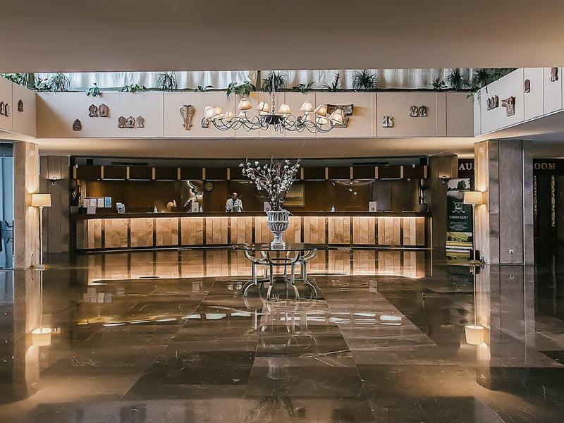 Große Hotel-Lobby mit glänzendem Marmorboden, zentralem Baum-Skulptur und einladendem Empfangstresen.