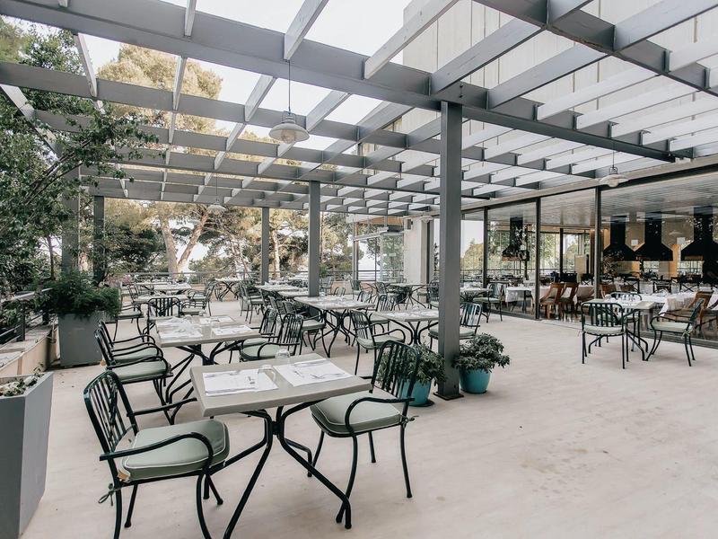 Moderner, offener Wintergarten mit schwarzem Metallgestell, Glasdach und grünen Stühlen.