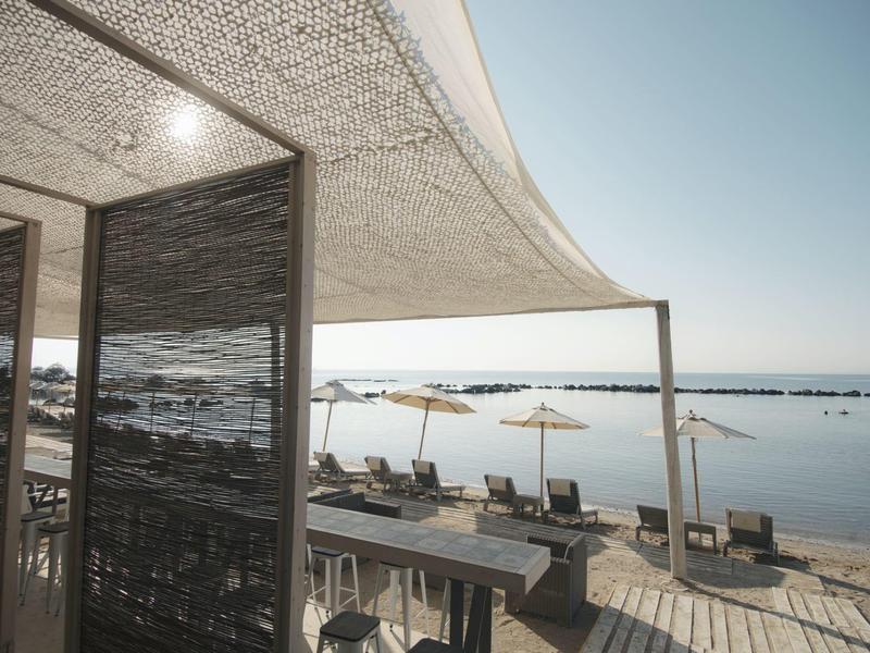 Terrasse mit Sonnenschirmen und Liegestühlen am Meer bei klarem Himmel, Holzbohlenboden.