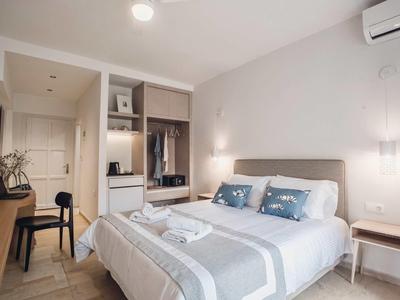 Camera d'hotel moderna con letto matrimoniale, scrivania, armadio aperto e arredi luminosi e neutri.