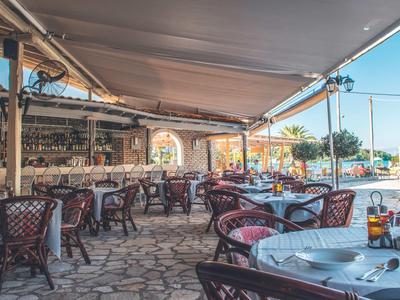 Accogliente terrazza esterna di un ristorante con tavoli apparecchiati e sedie in vimini sotto tende.