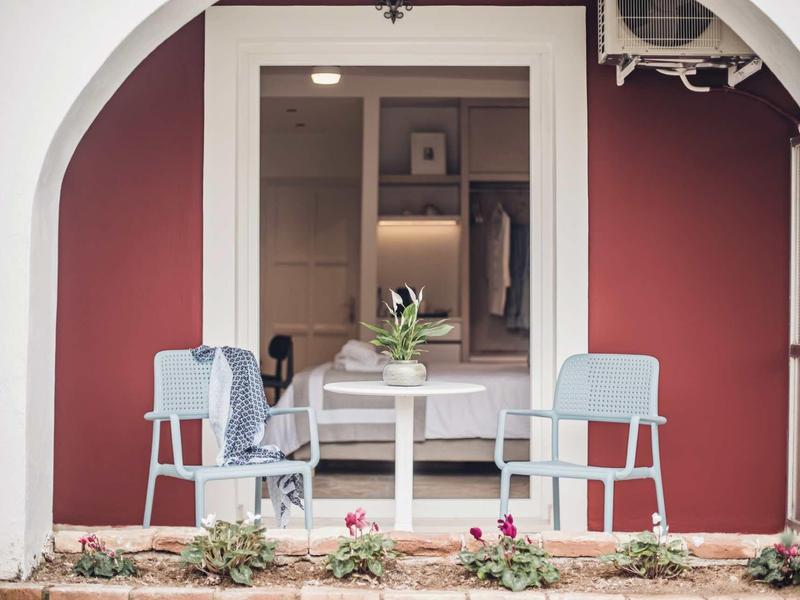 Dva židle a stůl s rostlinou před bordelovým domem s bílým obloukem.