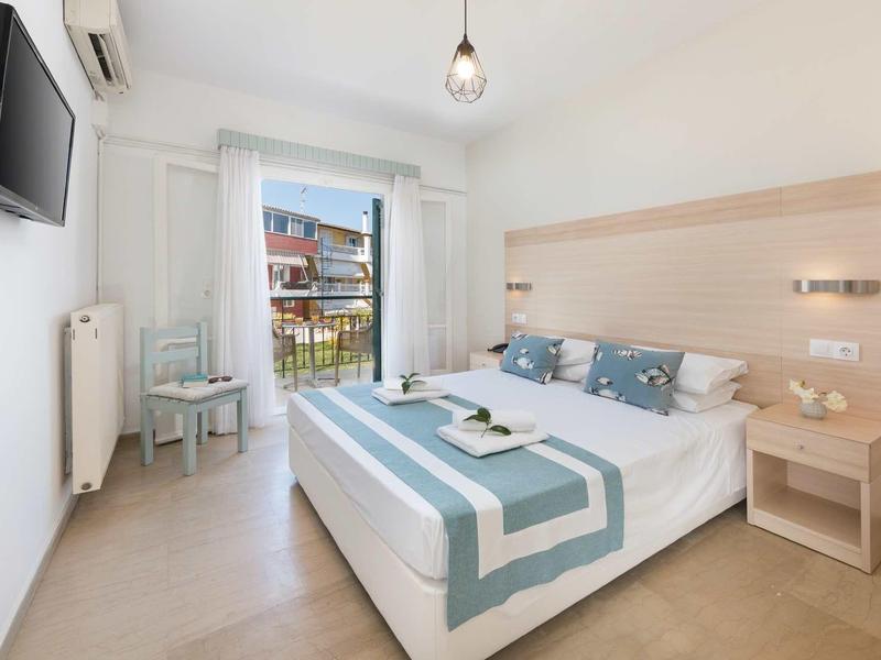 Světle zařízený hotelový pokoj s manželskou postelí, balkonem a moderním minimalistickým designem.