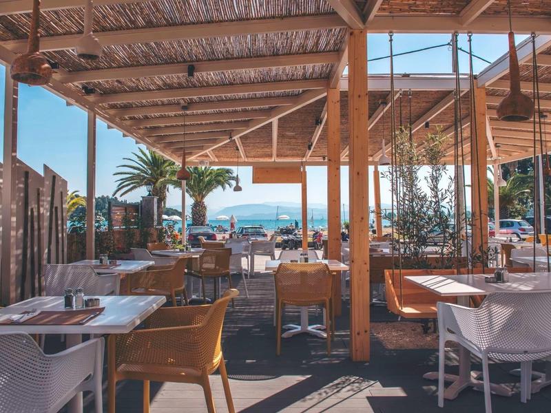 Otevřená restaurace s dřevěnou střechou a výhledem na moře za slunného počasí.