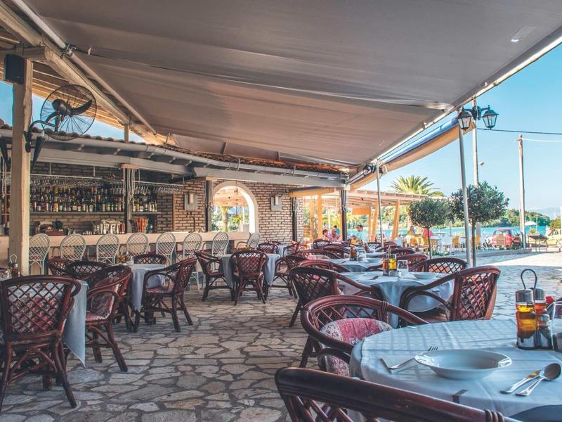 Zastřešená venkovní terasa restaurace s stoly a židlemi na dlážděné podlaze.