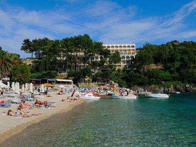 Zonnig strand met mensen die zonnen bij een beboste heuvel en hotel aan helder blauw water.