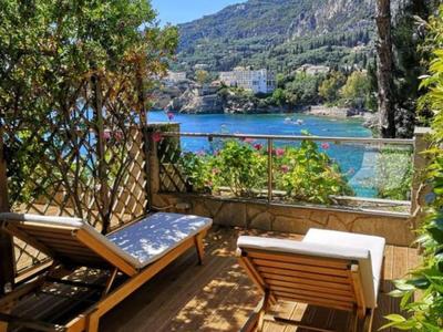 Tumbona en balcón con vista al mar y colinas verdes bajo cielo despejado.