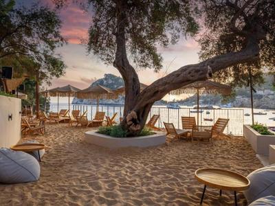 Área de playa con arena, asientos y vista al mar al atardecer.