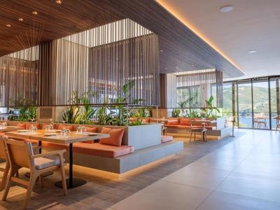 Restaurante moderno con detalles de madera, plantas y grandes ventanas con vista al paisaje.