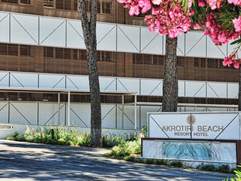 Buitensign voor Vakroti Beach Resort Hotel bij een gebouw met bloeiende roze bloemen