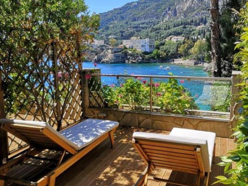 Zonnig terras met houten loungebanken en uitzicht op zee met kustplaats en bergen.