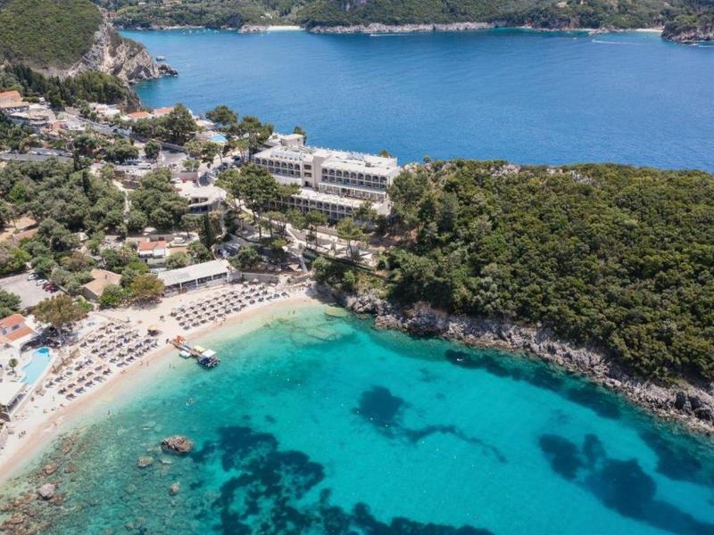 Luchtfoto van een kusthotel met strand, turquoise water en groen bos.