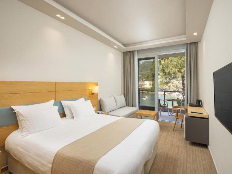 Moderne hotelkamer met een groot bed, balkon en lichte houten meubels in een neutraal kleurenpalet.