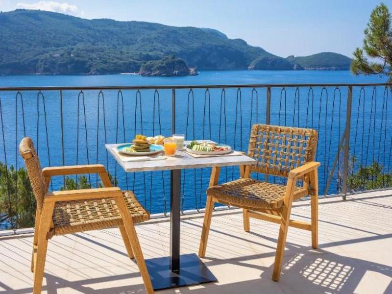 Terras met twee houten stoelen en een tafel met eten, uitzicht op blauwe zee en bergen.