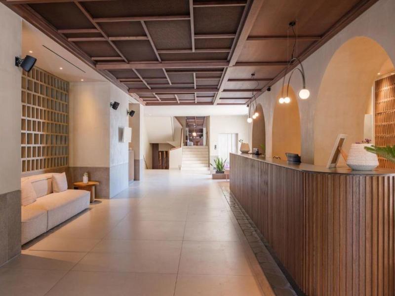 Ruime hotel lobby met houten balie, witte bank en warme verlichting onder een cassetteplafond.