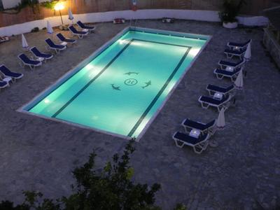 Illuminated rectangular pool surrounded by lounge chairs next to a wall in the evening.