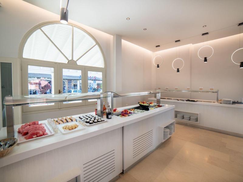 Moderní bufet s různými pokrmy v světlé, čisté místnosti s velkými okny.