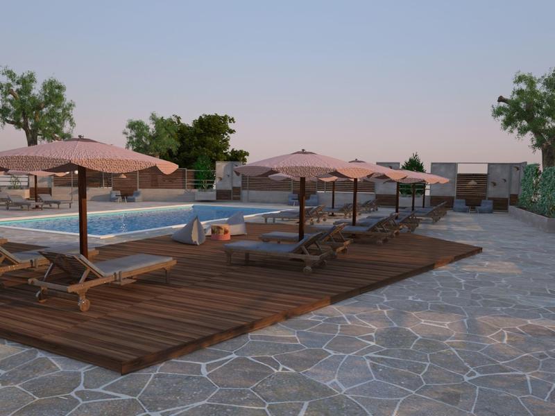 Bazénová zóna s lehátky a slunečníky na dřevěné terase a kamenné podlaze pod jasnou oblohou.