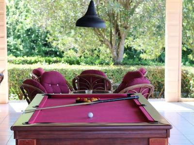 Red pool table outdoors with upholstered chairs and tree in the background.