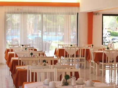 Bright dining room with white chairs and tables, orange tablecloths, and large windows.