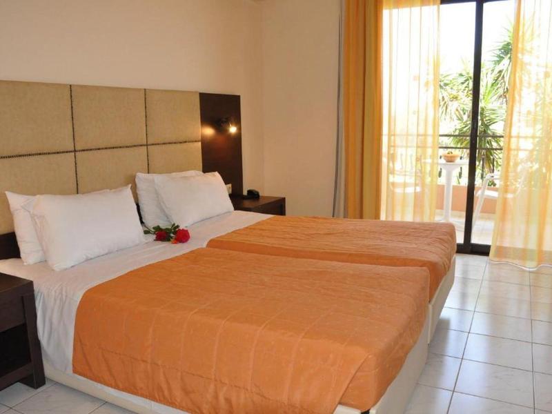 Zurückhaltend eingerichtetes Hotelzimmer mit zwei Einzelbetten und orangefarbenen Bettdecken.