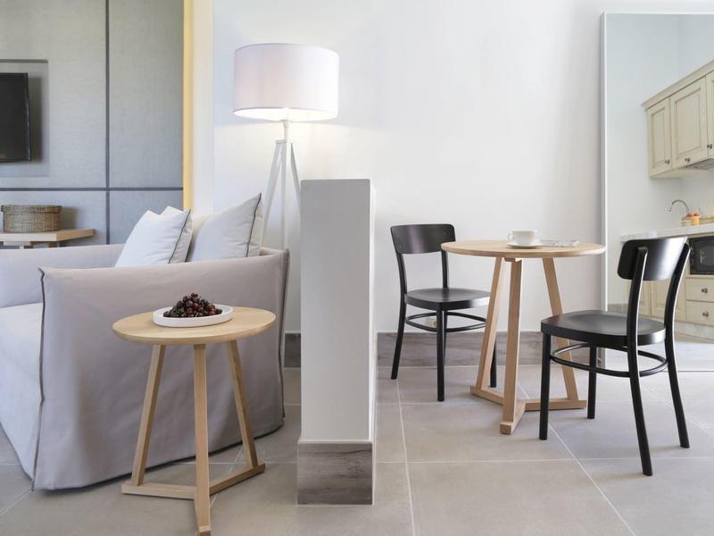 Jasny salon z białą sofą, małym drewnianym stolikiem i częścią jadalną z dwoma krzesłami.