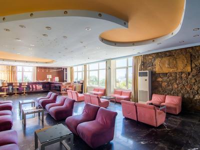 Salon d'hôtel lumineux avec fauteuils roses et grandes fenêtres.