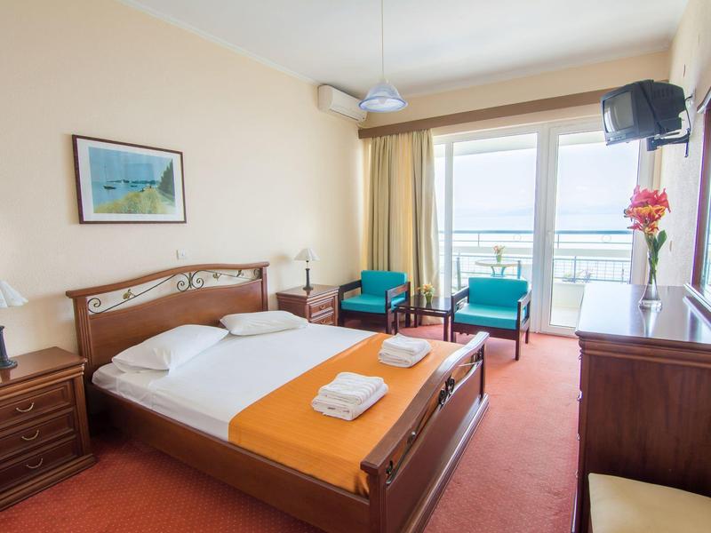 Hell eingerichtetes Schlafzimmer mit großem Bett, Holzmöbeln und Balkon mit Meerblick.