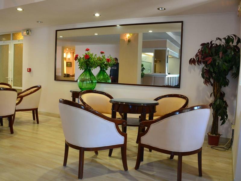 Gemütlicher Sitzbereich mit runden Stühlen, Holztisch, großem Spiegel und Pflanzen in hellem Raum.