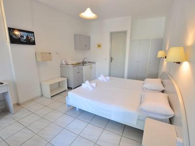 Lichte hotelkamer met tweepersoonsbed, kledingkast, tv en kitchenette in minimalistische stijl.