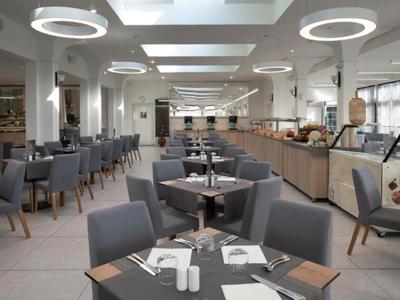 Moderne eetzaal met grijze stoelen, ronde tafels en buffetgebied onder ronde plafondlampen.