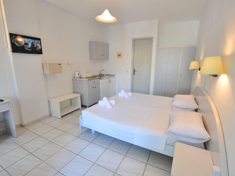 Lichte hotelkamer met tweepersoonsbed, kledingkast, tv en kitchenette in minimalistische stijl.