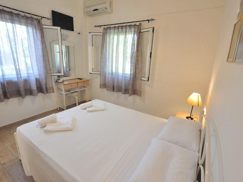 Een lichte slaapkamer met een tweepersoonsbed, witte muren en een klein bureau onder het raam.