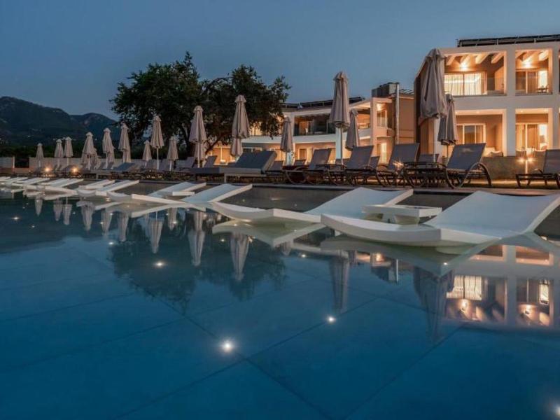 Hotel met verlicht zwembad en ligbedden bij schemering in een rustige omgeving.