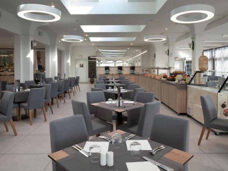 Moderne, lichte eetzaal met grijze stoelen en ronde plafondlampen.