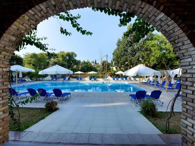 Blick durch einen Steinbogen auf einen blauen Pool mit Liegestühlen und weißen Sonnenschirmen im Freien.