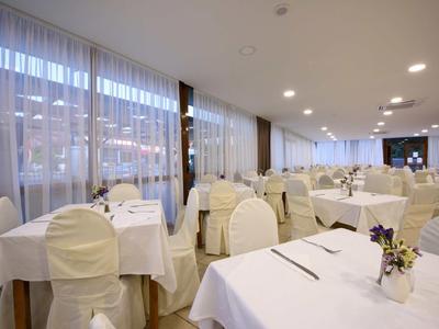 Heller, eleganter Speisesaal mit weiß gedeckten Tischen und Stühlen vor großen Fenstern.