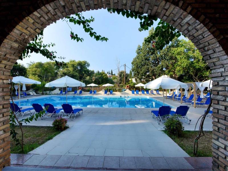 Uitzicht door een stenen boog op een zwembad met blauwe ligstoelen en witte parasols