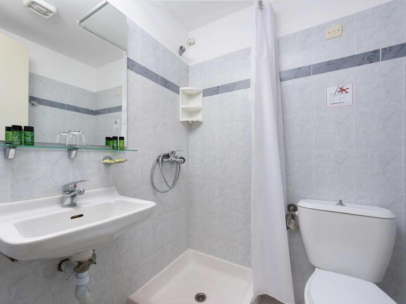 Compacte badkamer met douche, witte wastafel, toilet en lichtgrijze tegels.