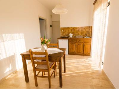 Zona pranzo luminosa con tavolo in legno, sedie e angolo cottura con piastrelle sul muro.