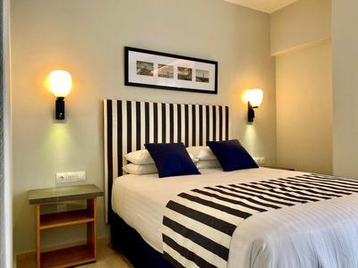 Camera d'hotel moderna con letto a righe, due cuscini blu e illuminazione a parete.