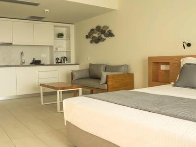 Modernes Hotelzimmer mit Bett, Sofa, Küchenzeile und minimalistischer Einrichtung.