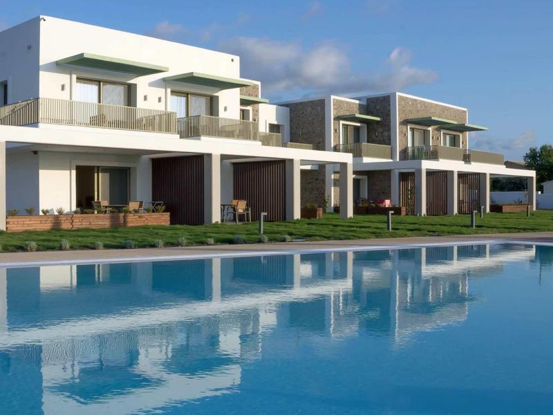 Moderne weiße Häuser mit Holzverkleidung spiegeln sich in großem blauen Pool bei klarem Himmel.