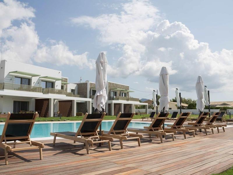 Moderne Poolanlage mit Liegestühlen und geschlossenen Sonnenschirmen bei wolkigem Himmel.