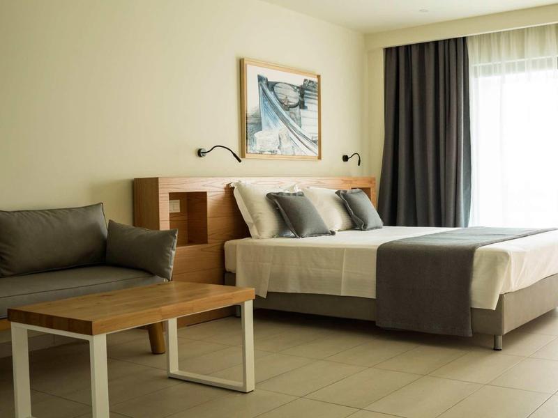 Modernes Schlafzimmer mit großem Bett, grauen Kissen, Holztisch und hellem Boden.