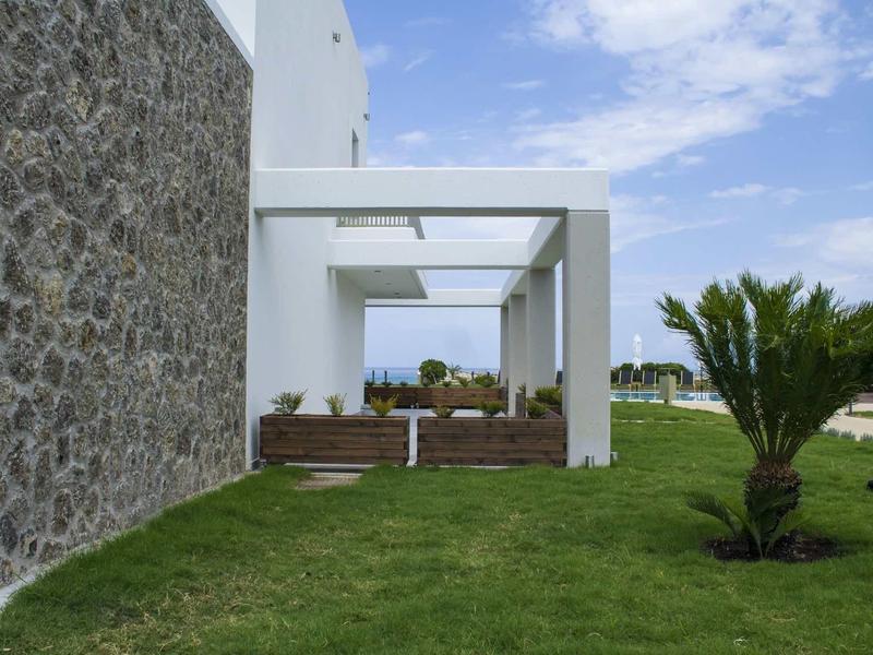 Modernes Haus mit weißer Fassade, Steinmauer, grüner Wiese und kleiner Palme im Garten.