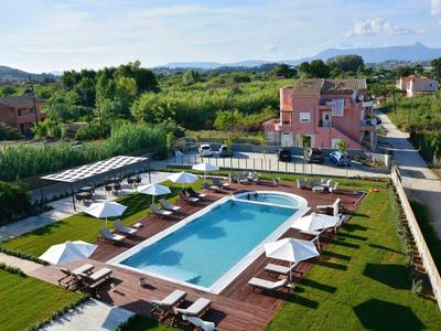 Moderner Außenpool mit Liegestühlen, Sonnenschirmen und grüner Wiese in einer ländlichen Umgebung.