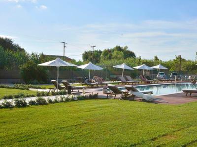 Grüner Rasen mit Pool, Holzdeck und weißen Sonnenschirmen an einem sonnigen Tag.